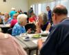 Congresswoman Clark sits and listens to a woman while attending a Senior Center luncheon.