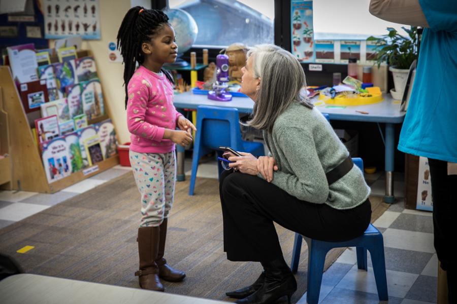 Rep. Clark kneels down and looks up a little girl while touring a child care center in Woburn.