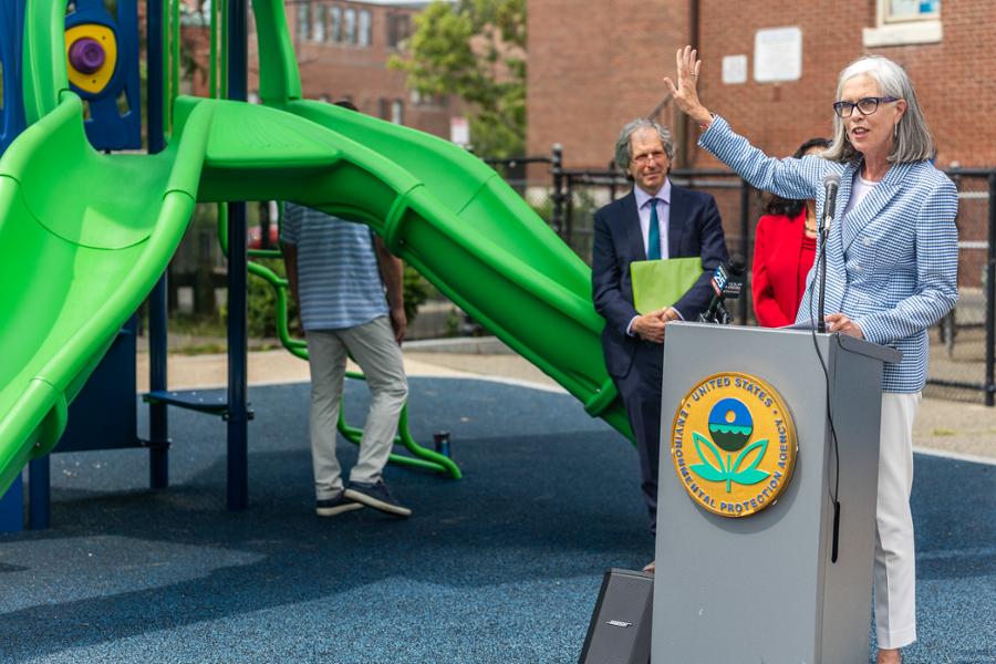 Rep. Clark is speaking at a podium with the Environmental Protection Agency seal on the front. She is gesturing to a playground.