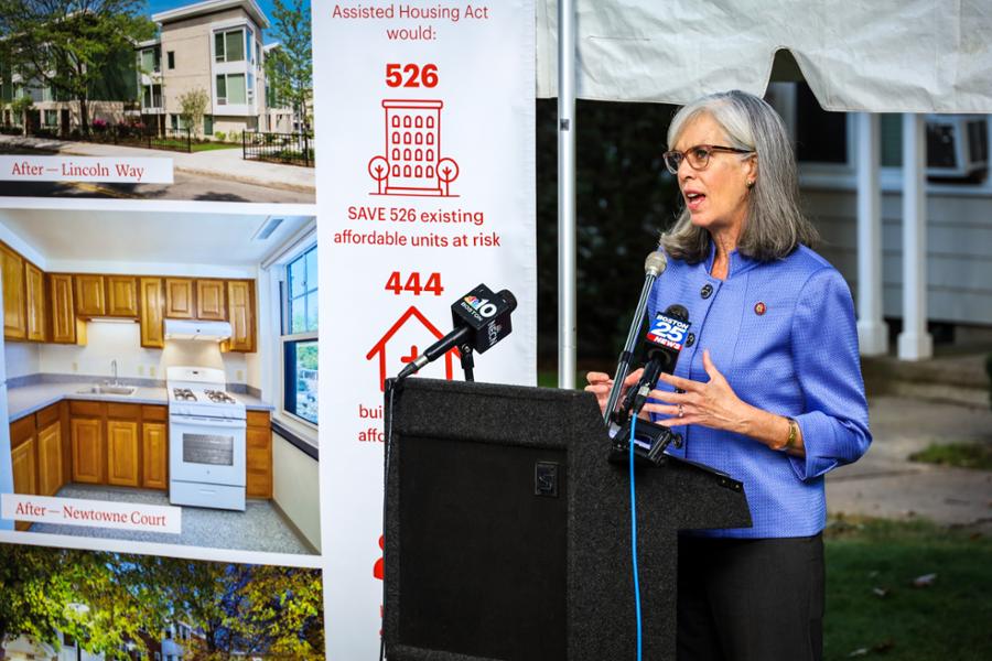 Rep. Clark is speaking at a podium in Cambridge with a big sign behind her about housing difficulties.
