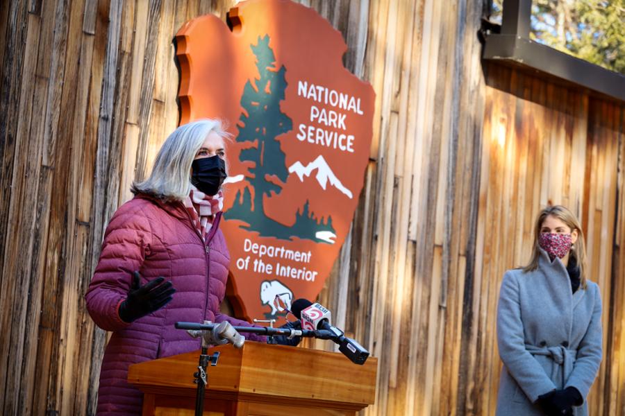 Rep. Clark is speaking at a podium in front of the seal of the National Park Service.
