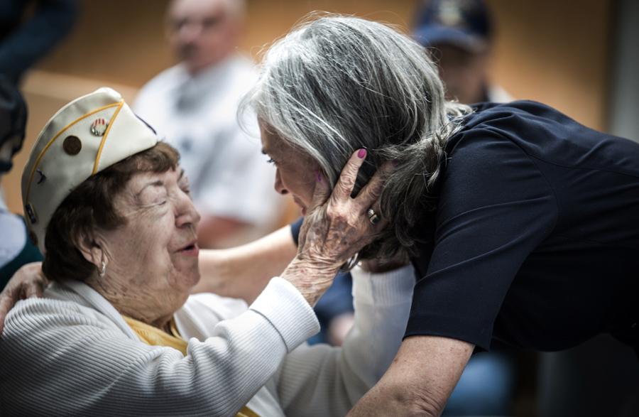 An elderly woman veterans holds Rep. Clark's face in her hands as Clark leans down to embrace the woman.