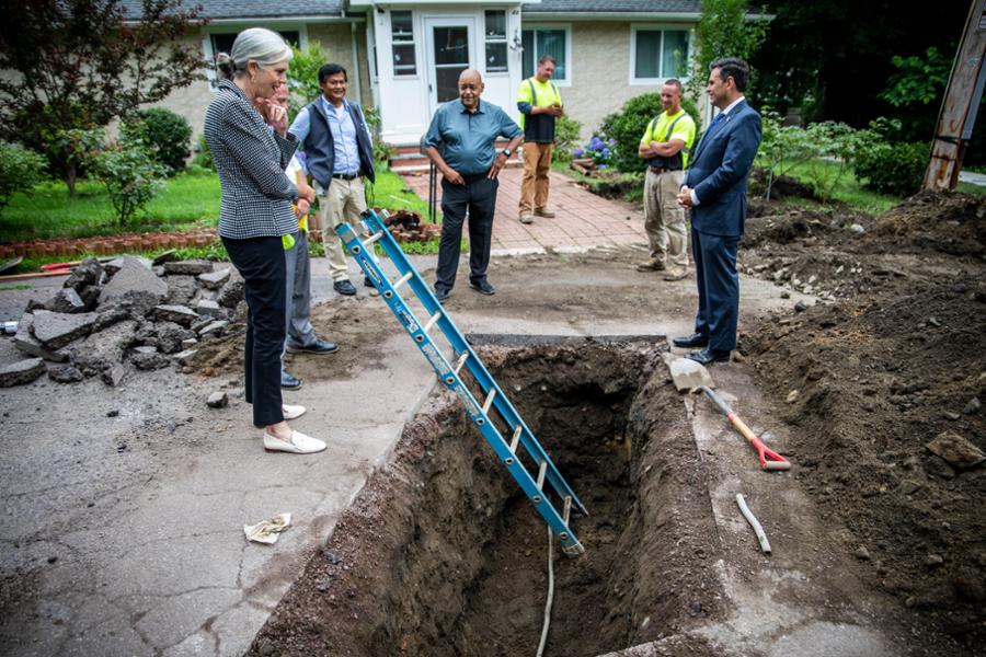 Rep. Clark looks in a hole with a ladder coming out of it, the site of a lead pipe being replaced at a Malden home.